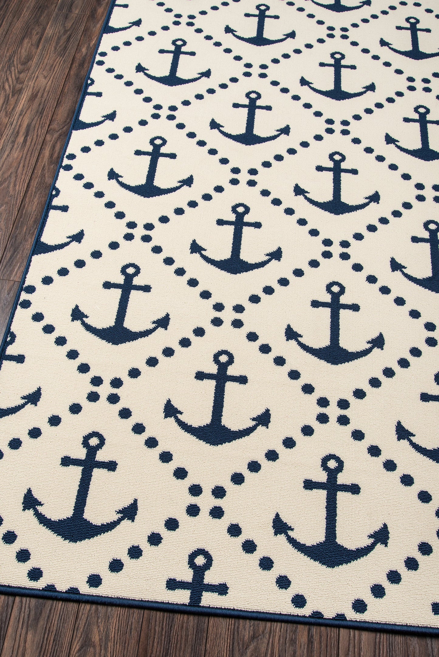Navy anchor-pattern rug, 7' x 10', on white with dotted diamond borders and blue edge on a wooden floor.