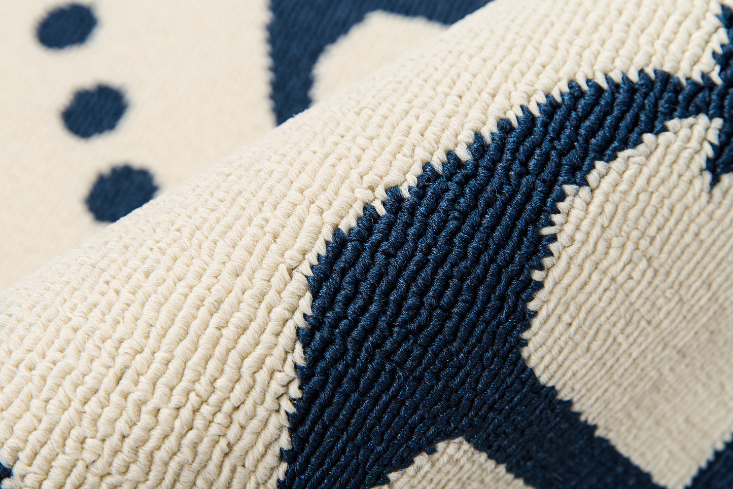 Close-up of a beige rug with navy blue geometric pattern; thick looped pile and textured weave
