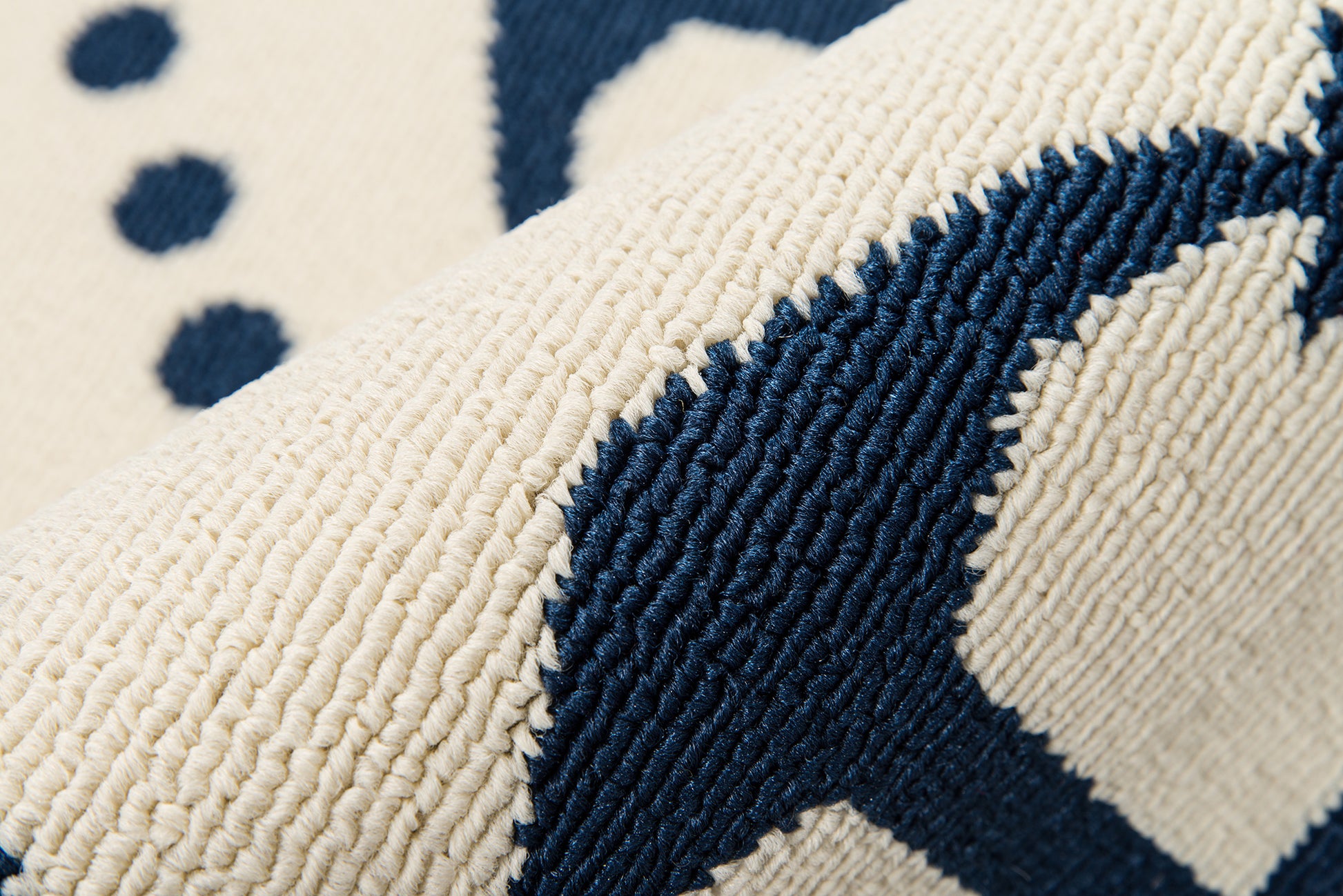 Close-up of a beige rug with navy blue geometric pattern; thick looped pile and textured weave
