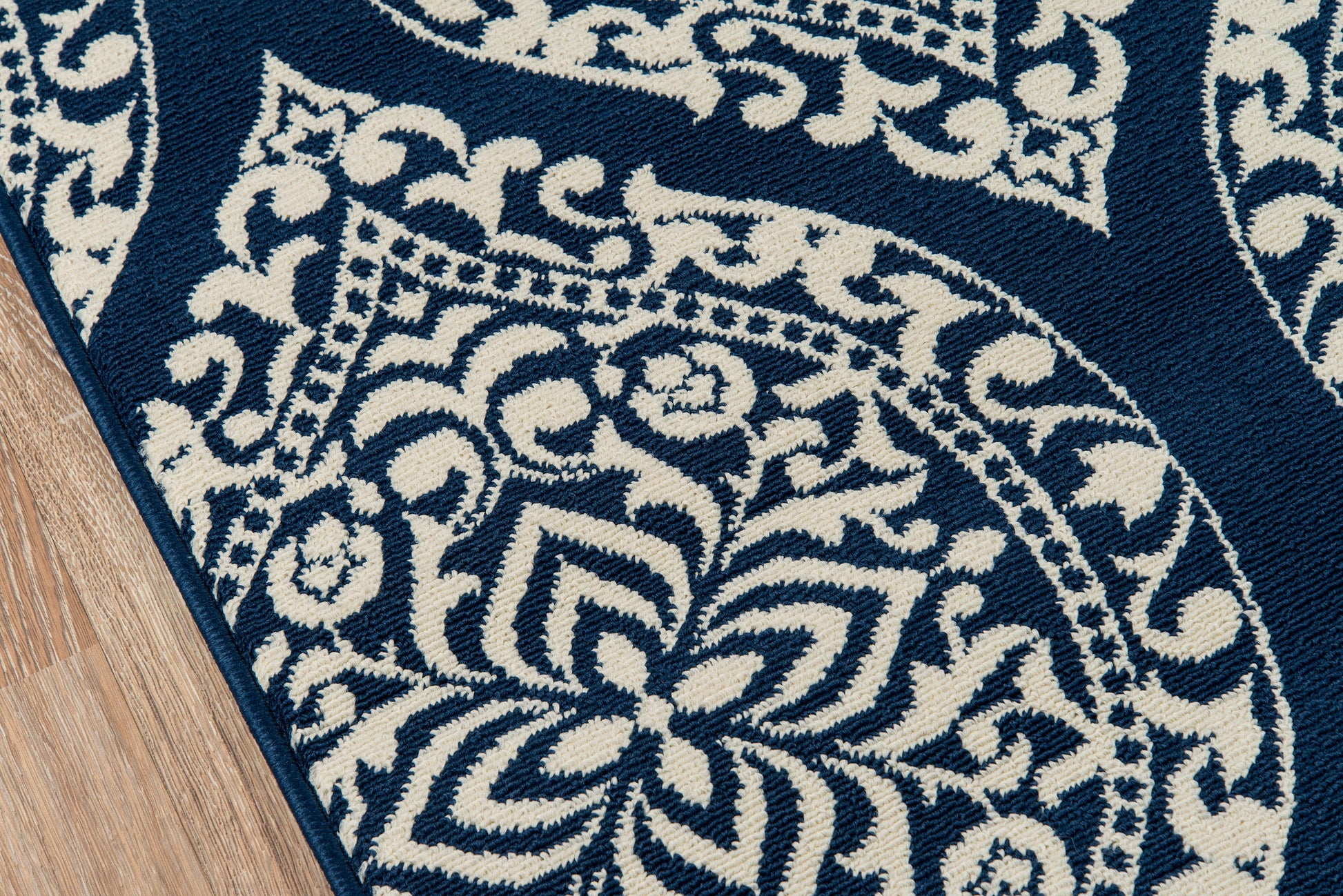 Navy blue rug with cream ornate floral and medallion pattern, wood floor edge visible.