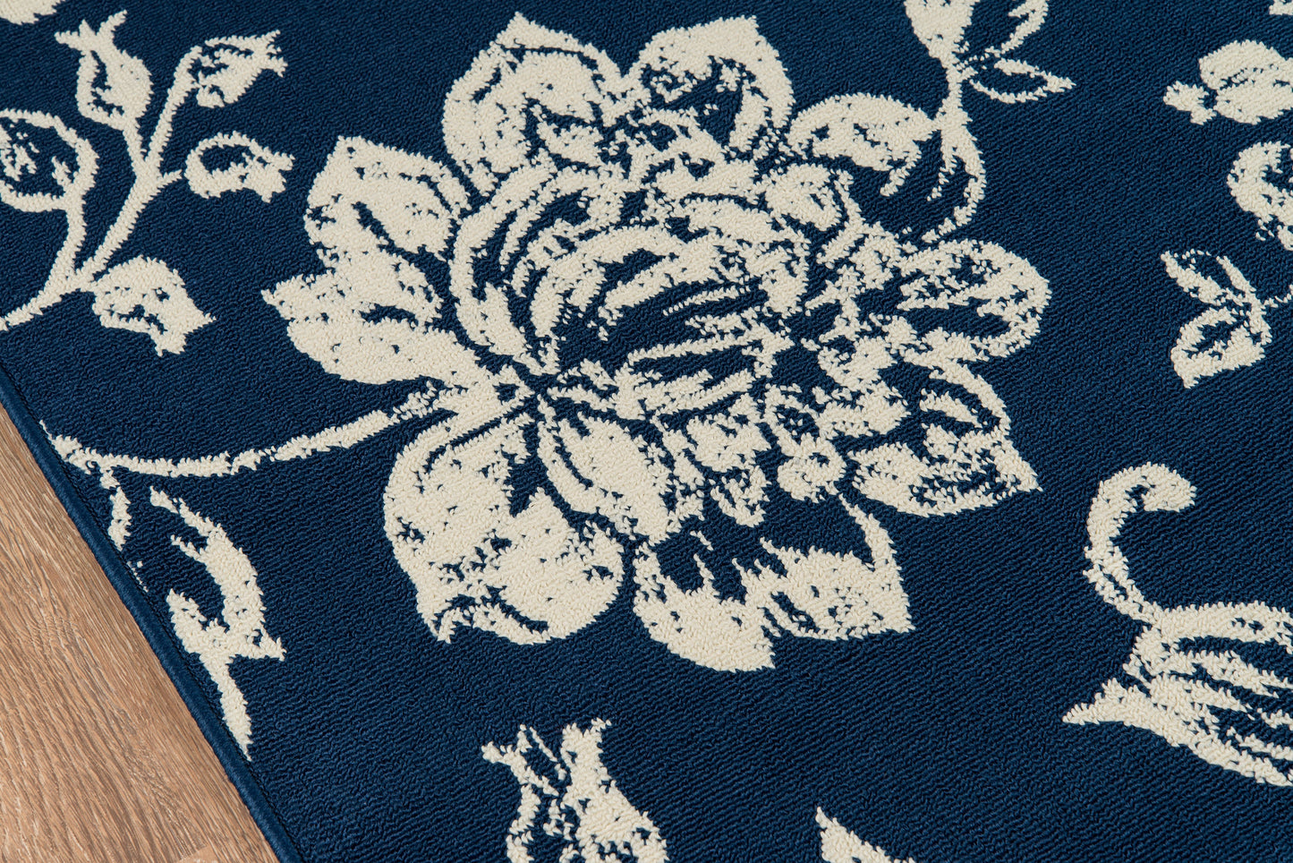 Navy blue rug with large white floral pattern; corner edge on wood floor.