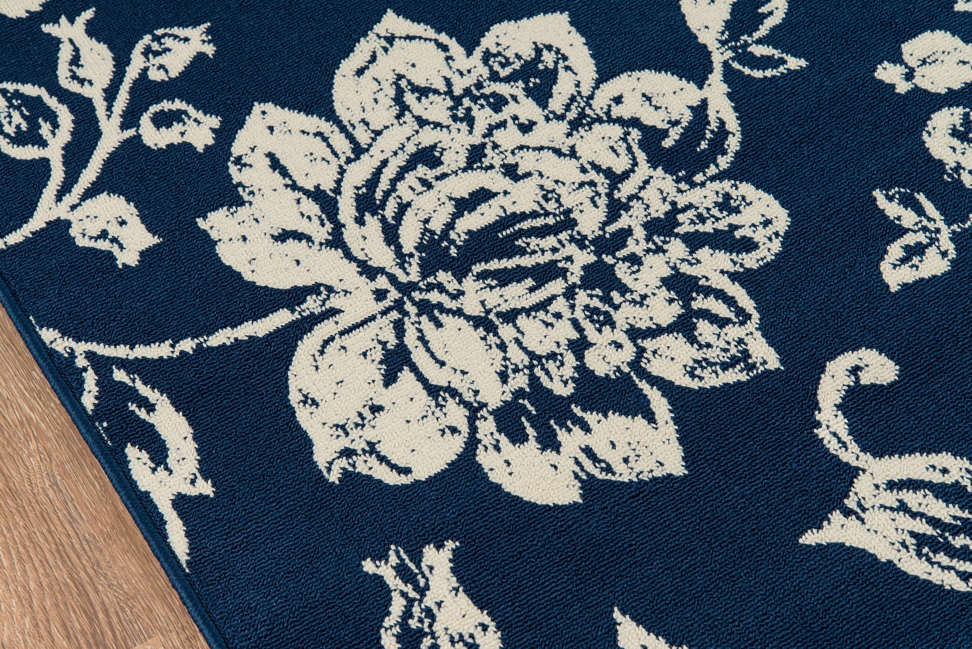 Navy blue rug with large white floral pattern; corner edge on wood floor.