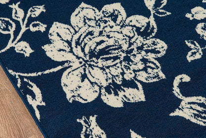 Navy blue rug with large white floral pattern; corner edge on wood floor.