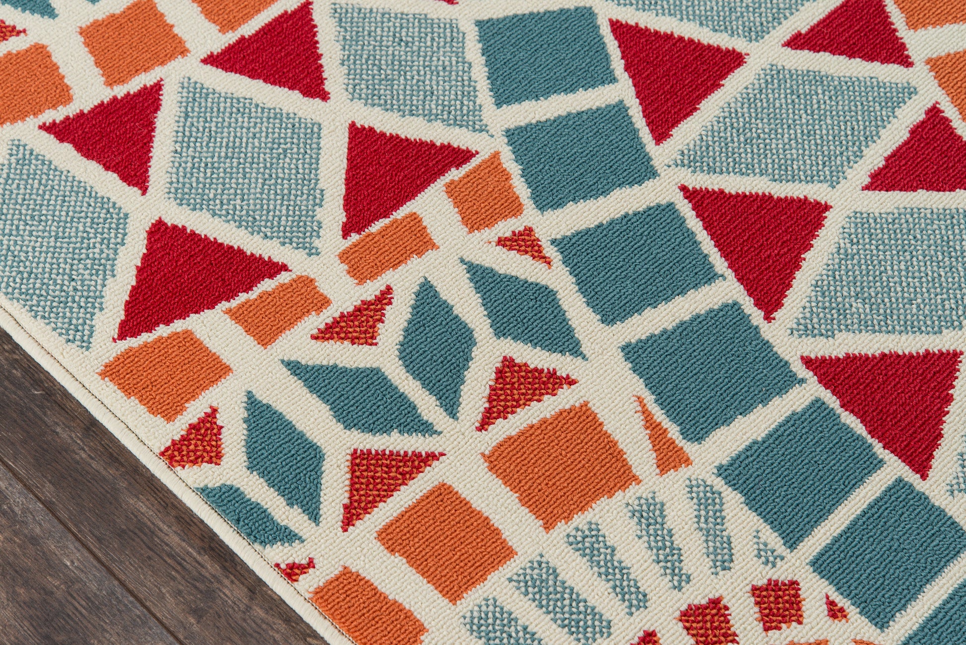 Woven area rug with geometric mosaic of red, teal, and orange triangles and squares on a wooden floor.