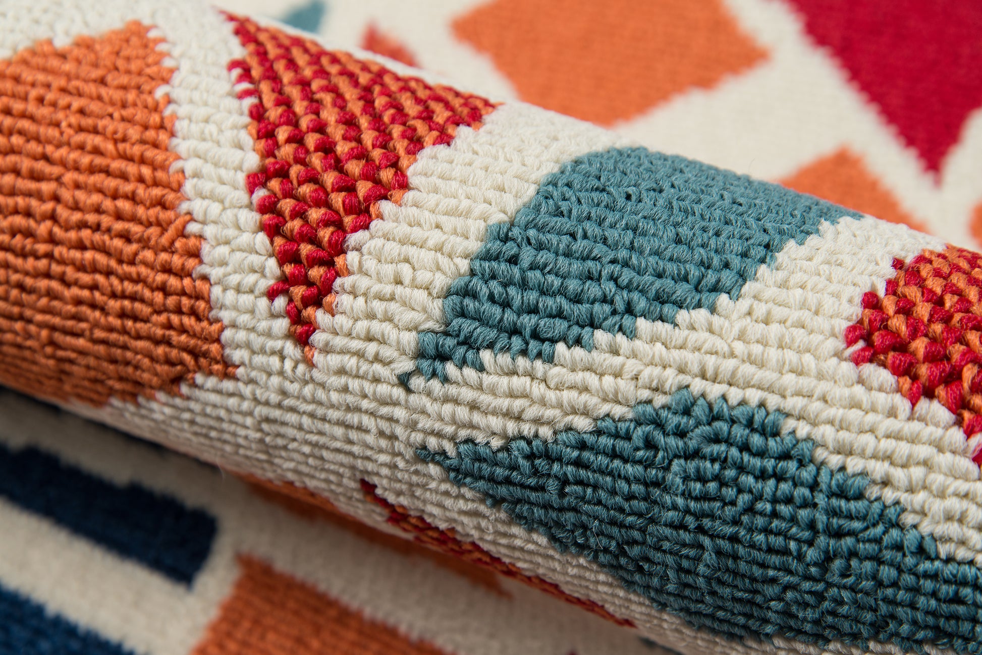 Rolled kilim-style rug with bold geometric orange, teal, red and white patterns, thick woven texture.