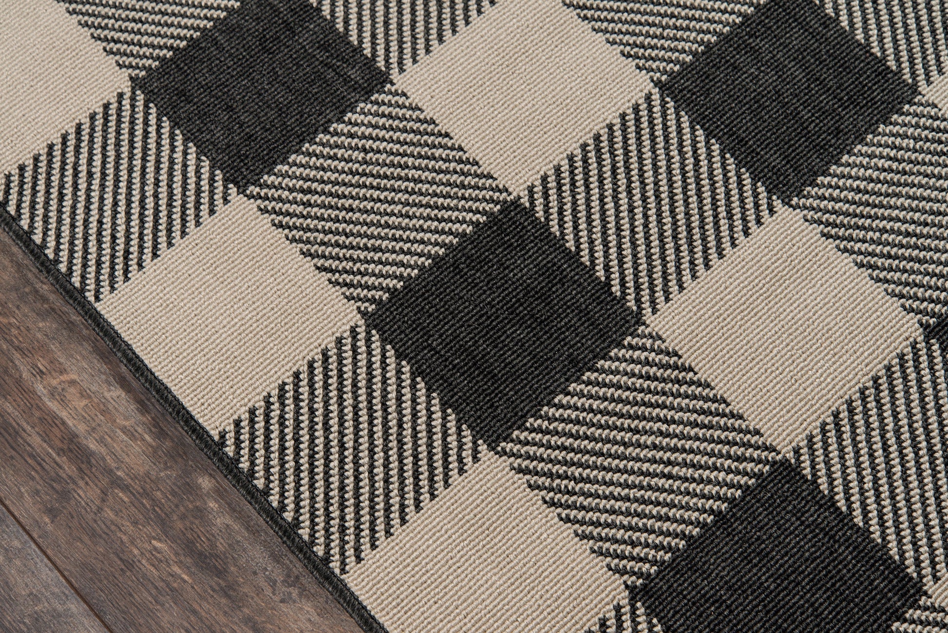 Buffalo-check rug in black and beige, woven textile with a dark border on wood floor.