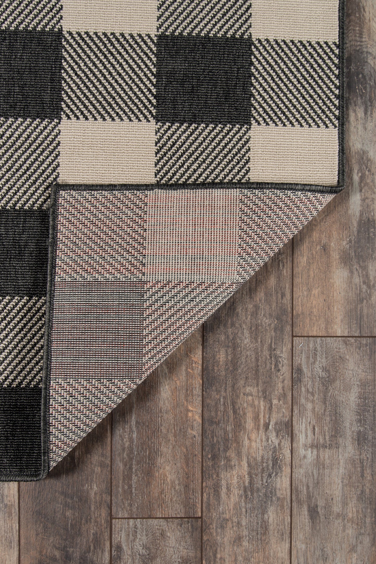 Beige and black checkerboard woven rug with a folded corner exposing the underside on wood flooring.