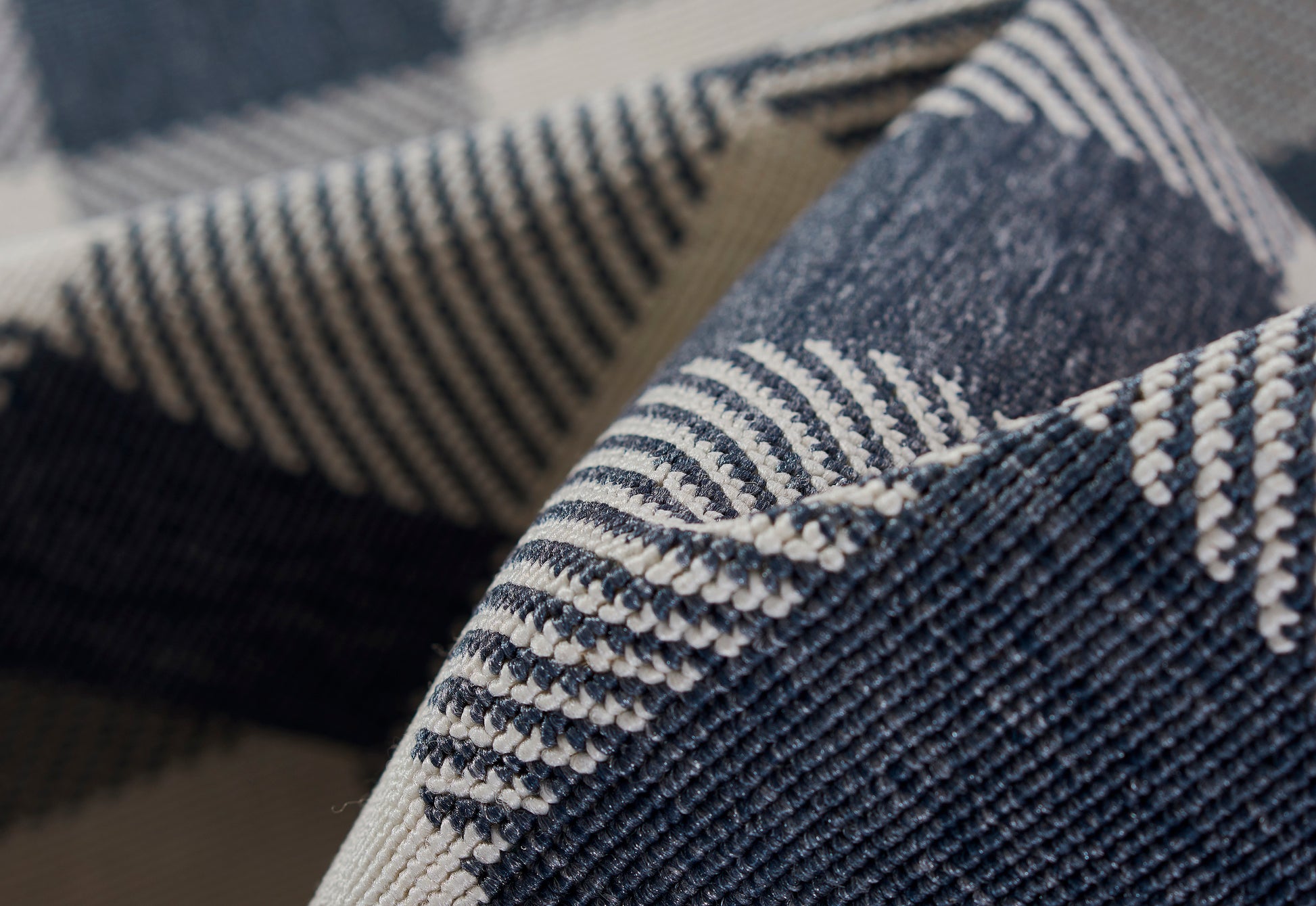 Indigo denim twill close-up with white contrast stitching; folded rugged fabric for casual wear.