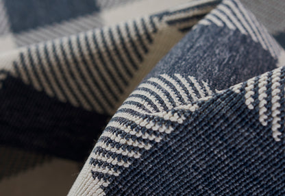 Indigo denim twill close-up with white contrast stitching; folded rugged fabric for casual wear.