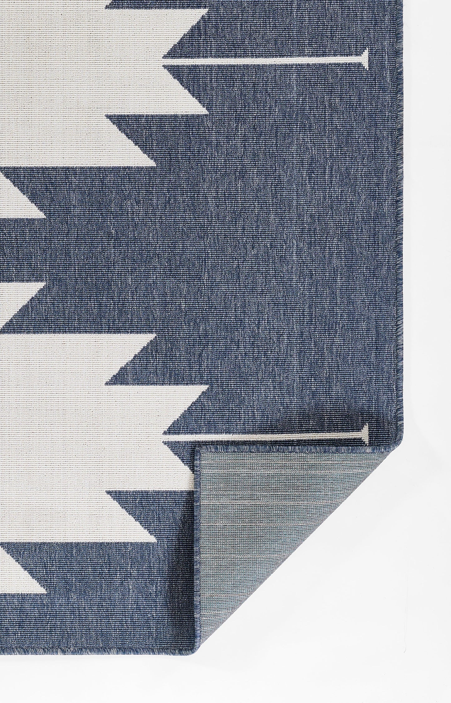 Blue woven rug with white chevron zigzag pattern; folded corner reveals grey backing and clean edge.