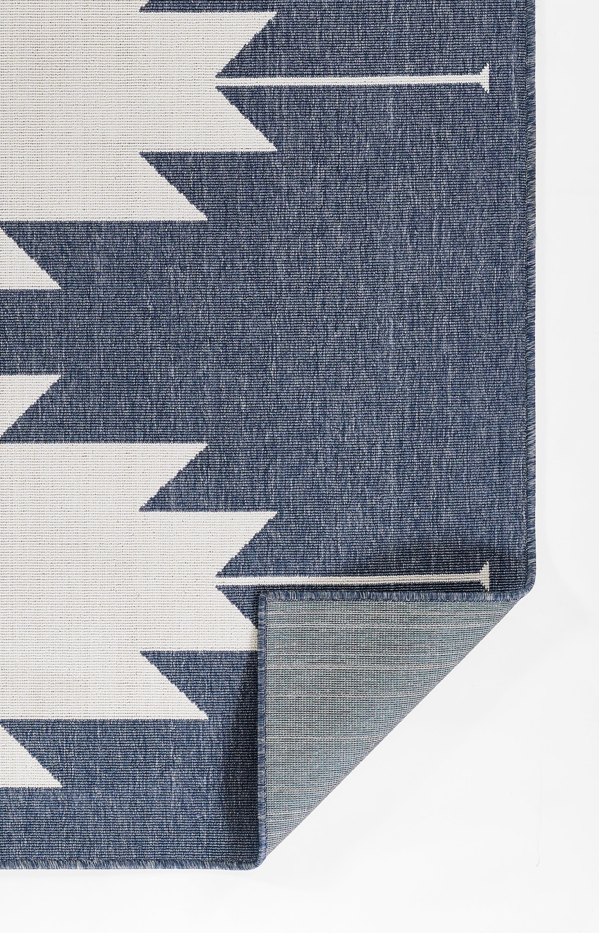 Blue woven rug with white chevron zigzag pattern; folded corner reveals grey backing and clean edge.