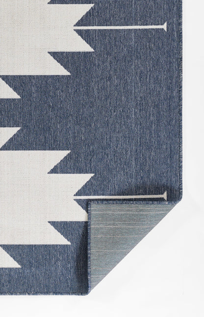 Blue woven rug with white chevron zigzag pattern; folded corner reveals grey backing and clean edge.