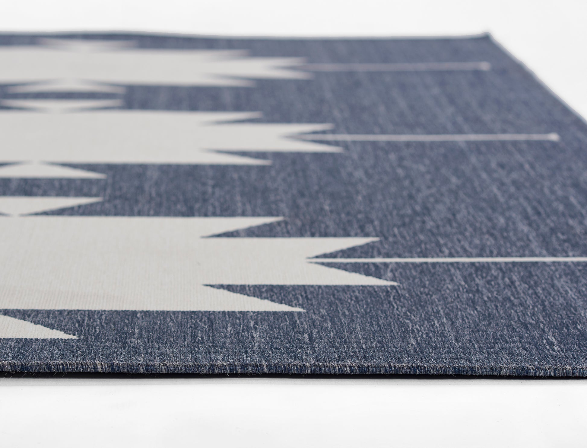 Navy blue woven rug with bold light-gray chevron pattern; close-up textured weave.