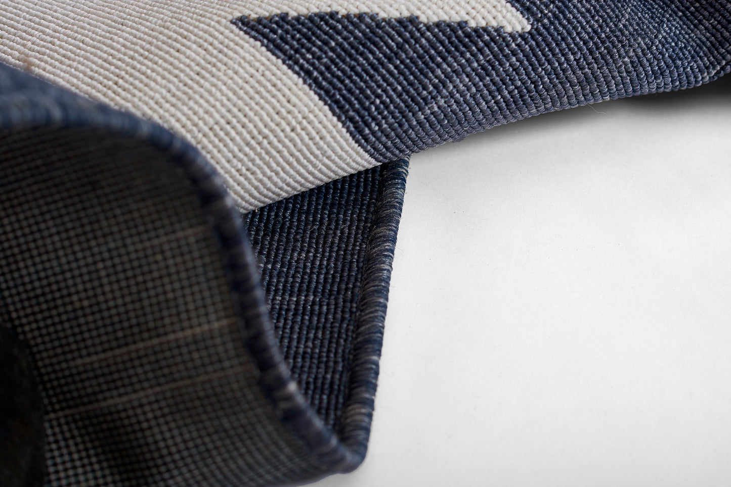 Woven navy & light gray geometric rug, folded corner reveals plaid underside.
