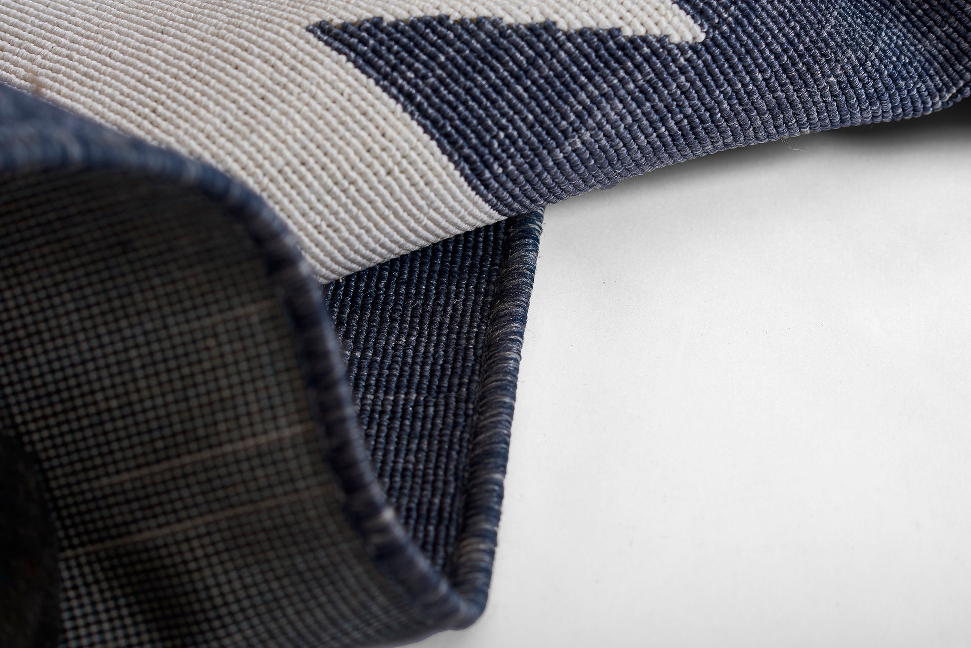 Woven navy & light gray geometric rug, folded corner reveals plaid underside.