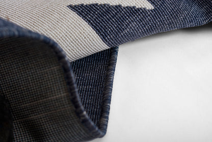 Woven navy & light gray geometric rug, folded corner reveals plaid underside.