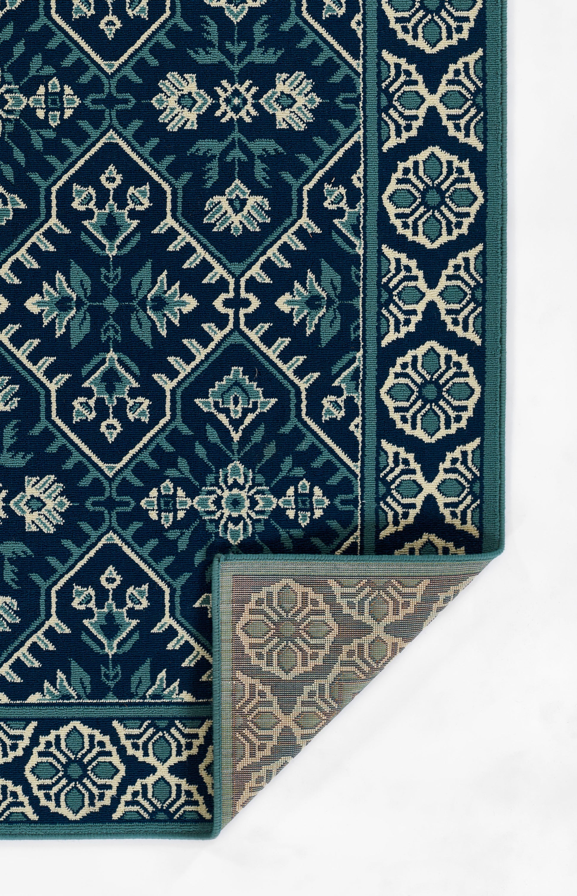 Ornate teal and ivory oriental rug with geometric lattice, floral motifs and border; folded corner shows beige underside
