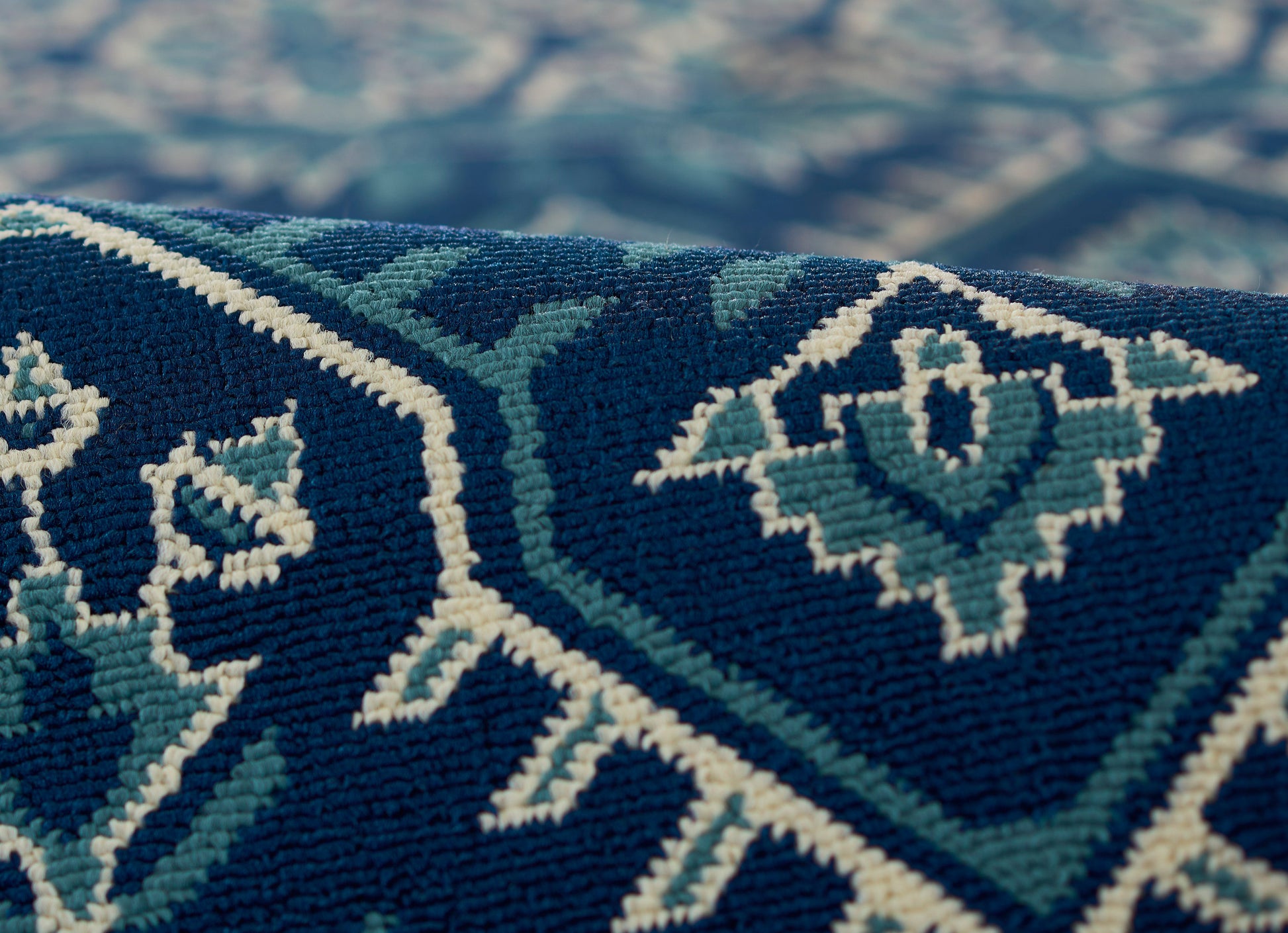 Close-up of a navy blue woven rug with teal and white diamond patterns and a textured geometric design.