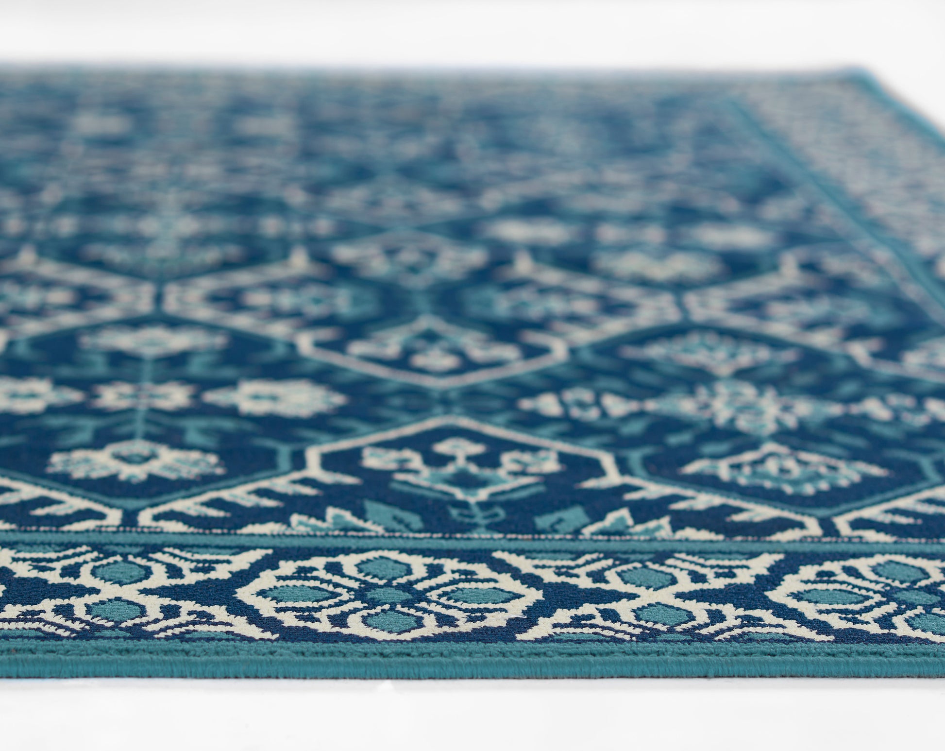 Teal-blue geometric area rug with white motifs and a patterned border, angled close-up.