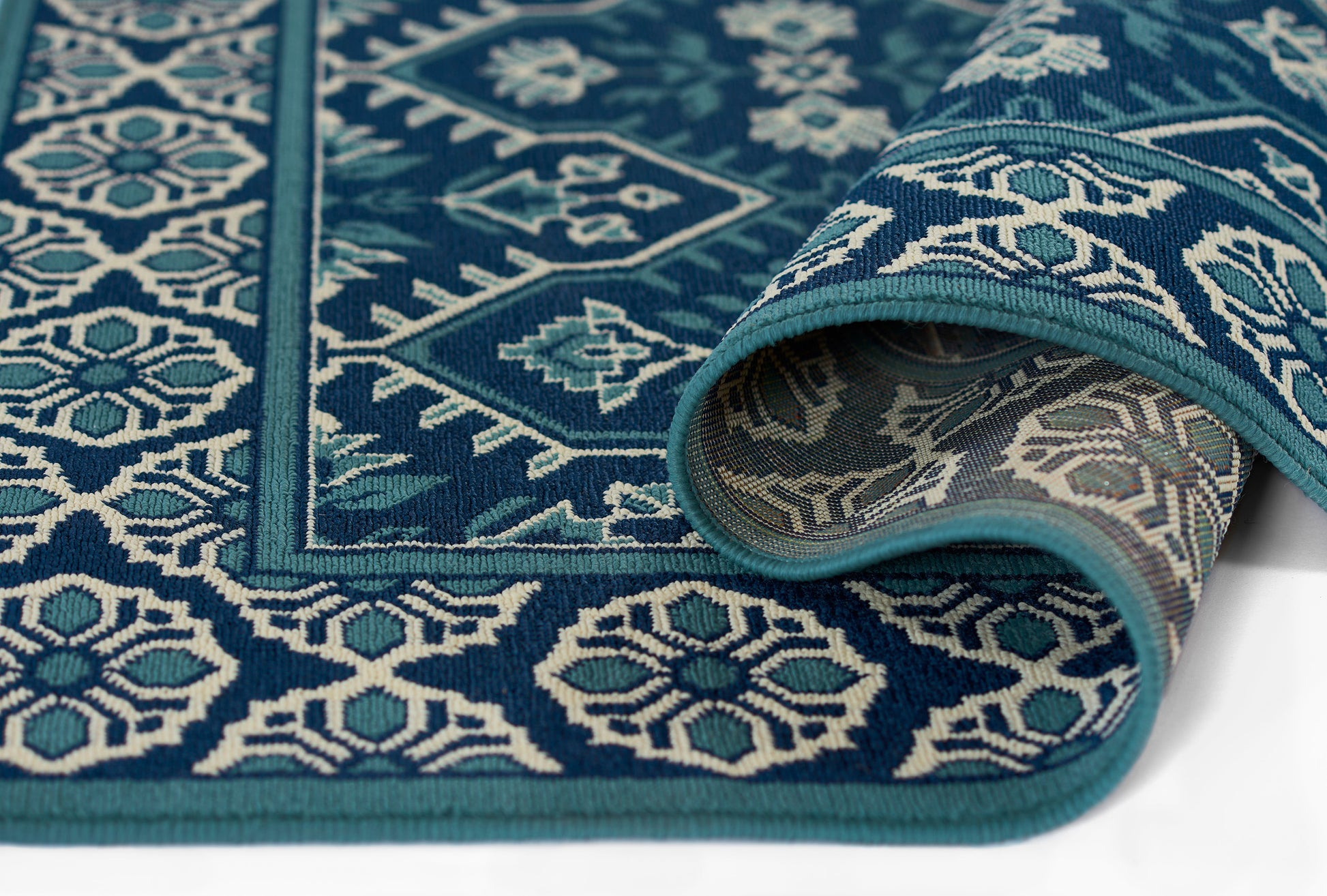 Deep teal and blue kilim-style rug with white geometric motifs, folded edge showing underside.