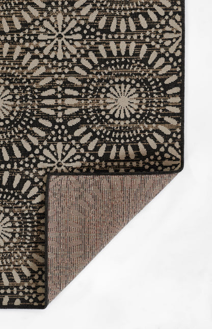 Black patterned rug with beige sunburst motifs; folded corner reveals brown underside, rustic boho textile.