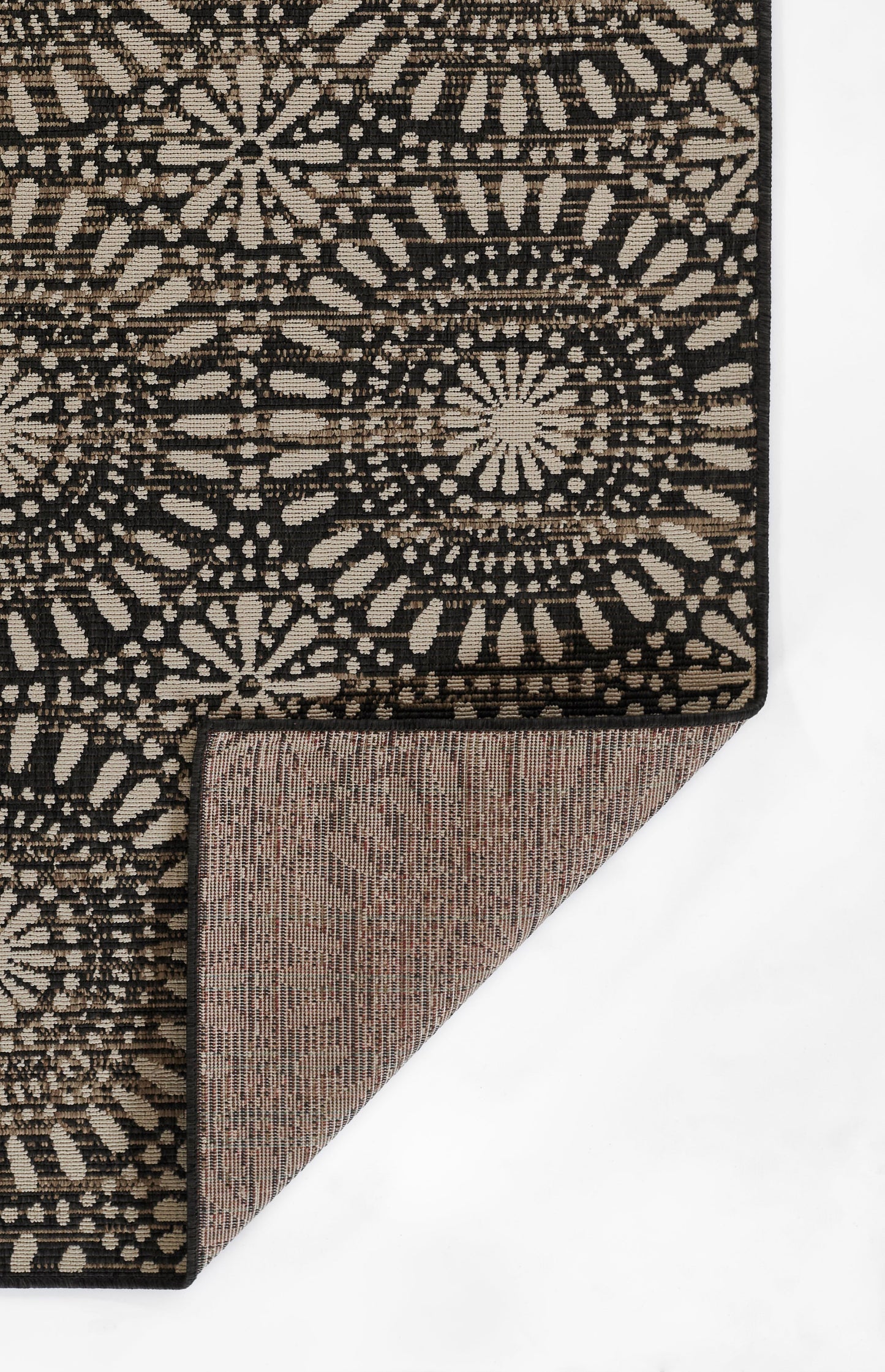 Boho-style black and beige rug with circular medallion motifs; folded corner reveals brown woven backing.
