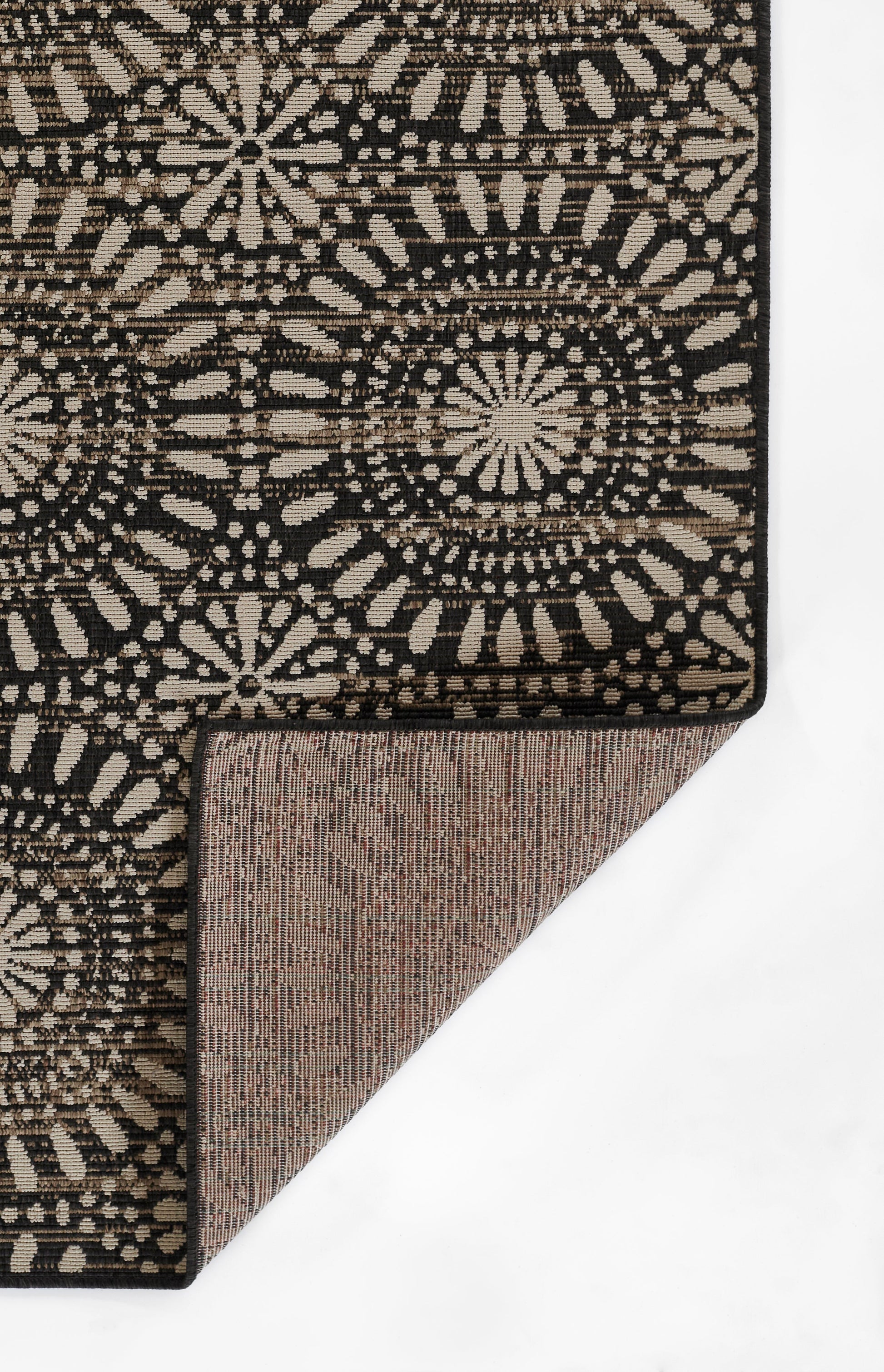 Boho-style black and beige rug with circular medallion motifs; folded corner reveals brown woven backing.