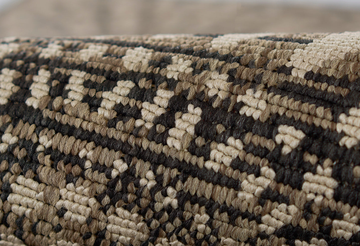 Close-up of a tufted woven rug with beige, brown and black geometric diamonds; earthy kilim-style textile.