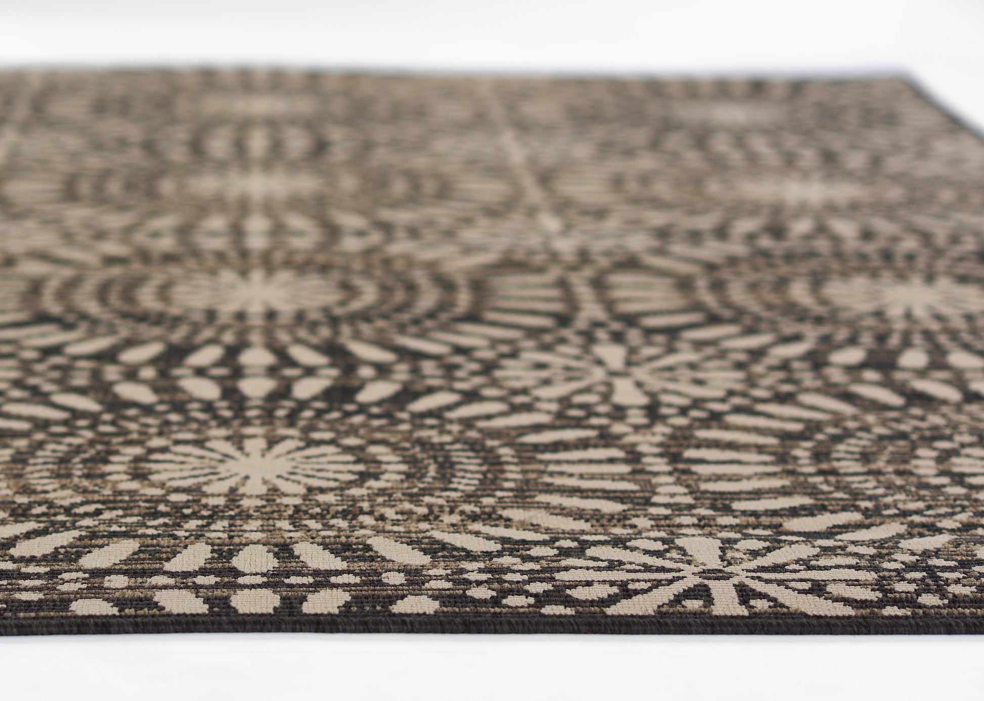 Rectangular rug with black and beige geometric mandala-like circular pattern, woven texture.