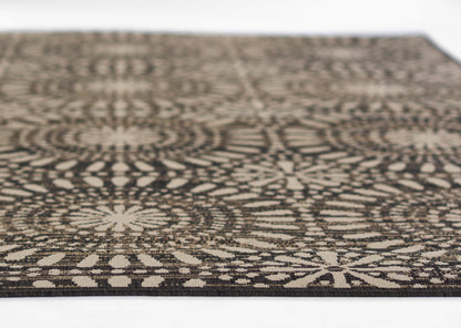 Rectangular rug with black and beige geometric mandala-like circular pattern, woven texture.