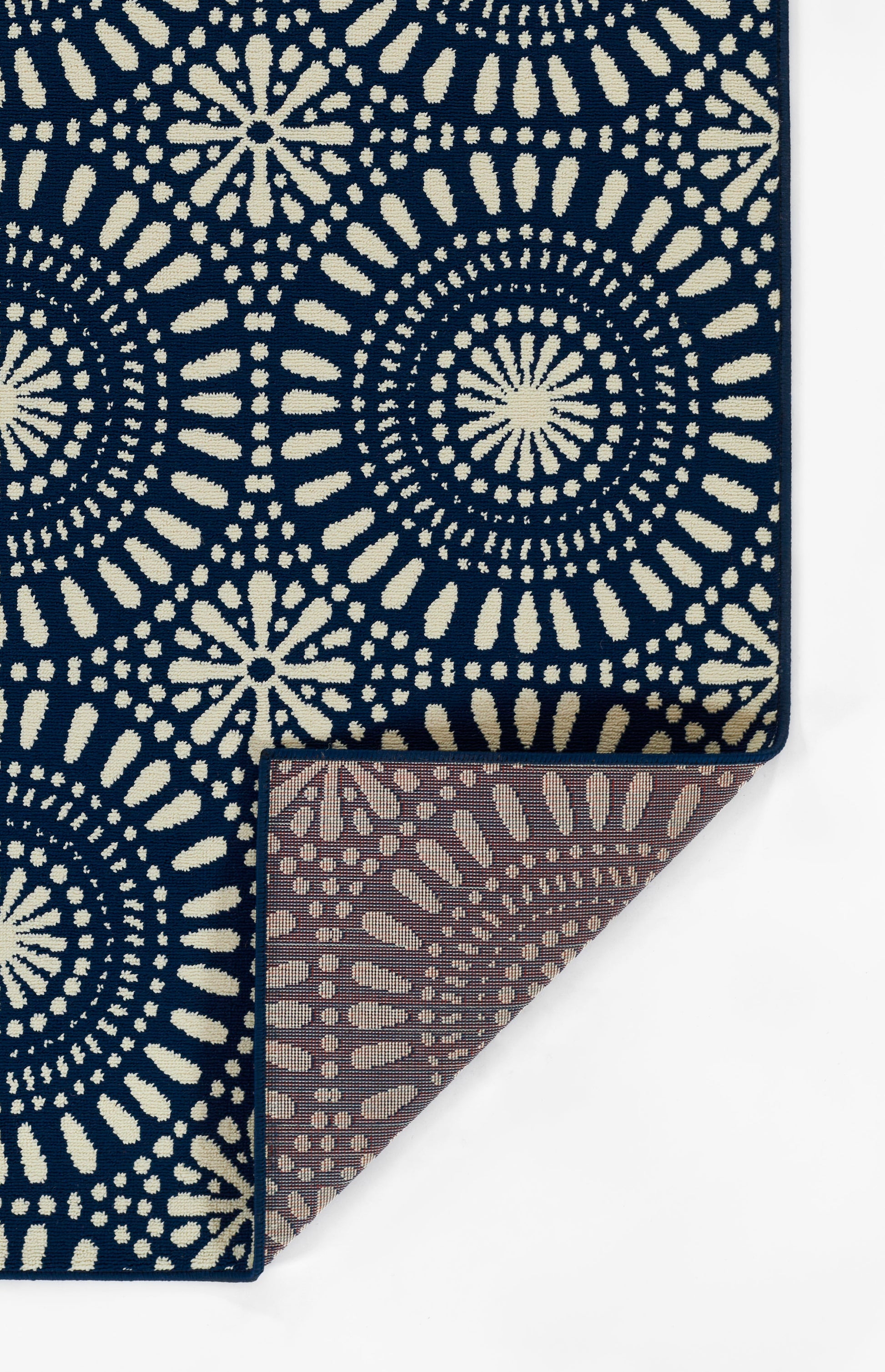 Navy blue rug with cream circular mandala and sunburst motifs; folded corner reveals brown reverse.