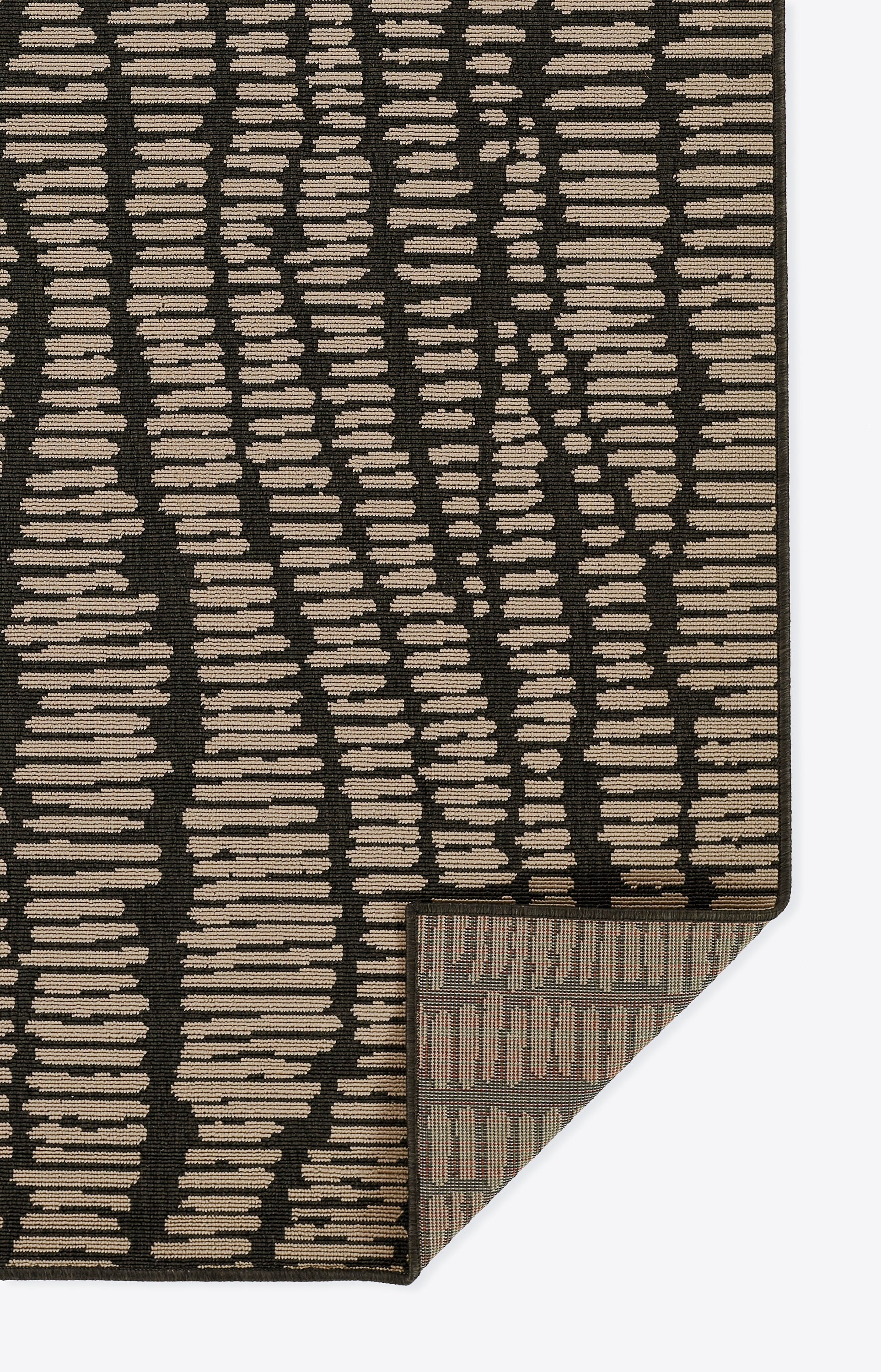 Rectangular rug with black background and irregular beige horizontal dashes; textured weave, folded corner reveals underside.