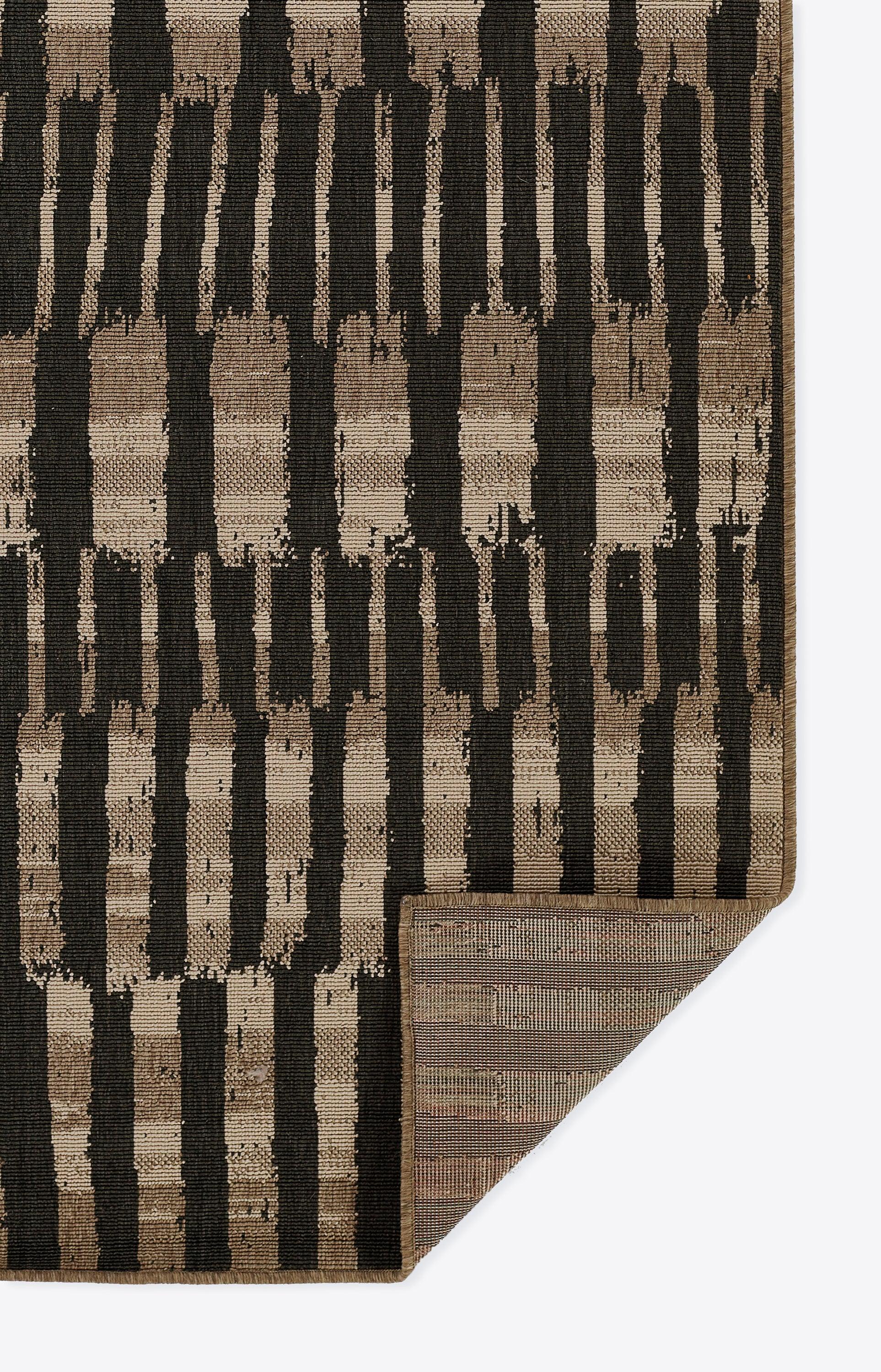 Brown and black geometric area rug with vertical brush-stroke stripes; folded corner shows rug backing.