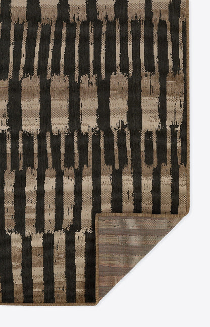 Brown and black geometric area rug with vertical brush-stroke stripes; folded corner shows rug backing.