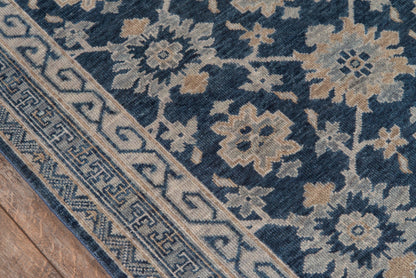 Navy blue oriental rug with beige floral medallions and a geometric Greek-key border on a wooden floor.