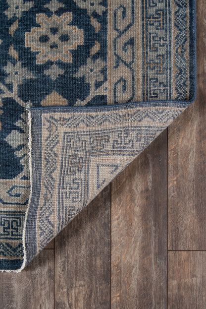 Blue and beige oriental rug with floral medallions and Greek-key border, folded to show underside on wood floor.