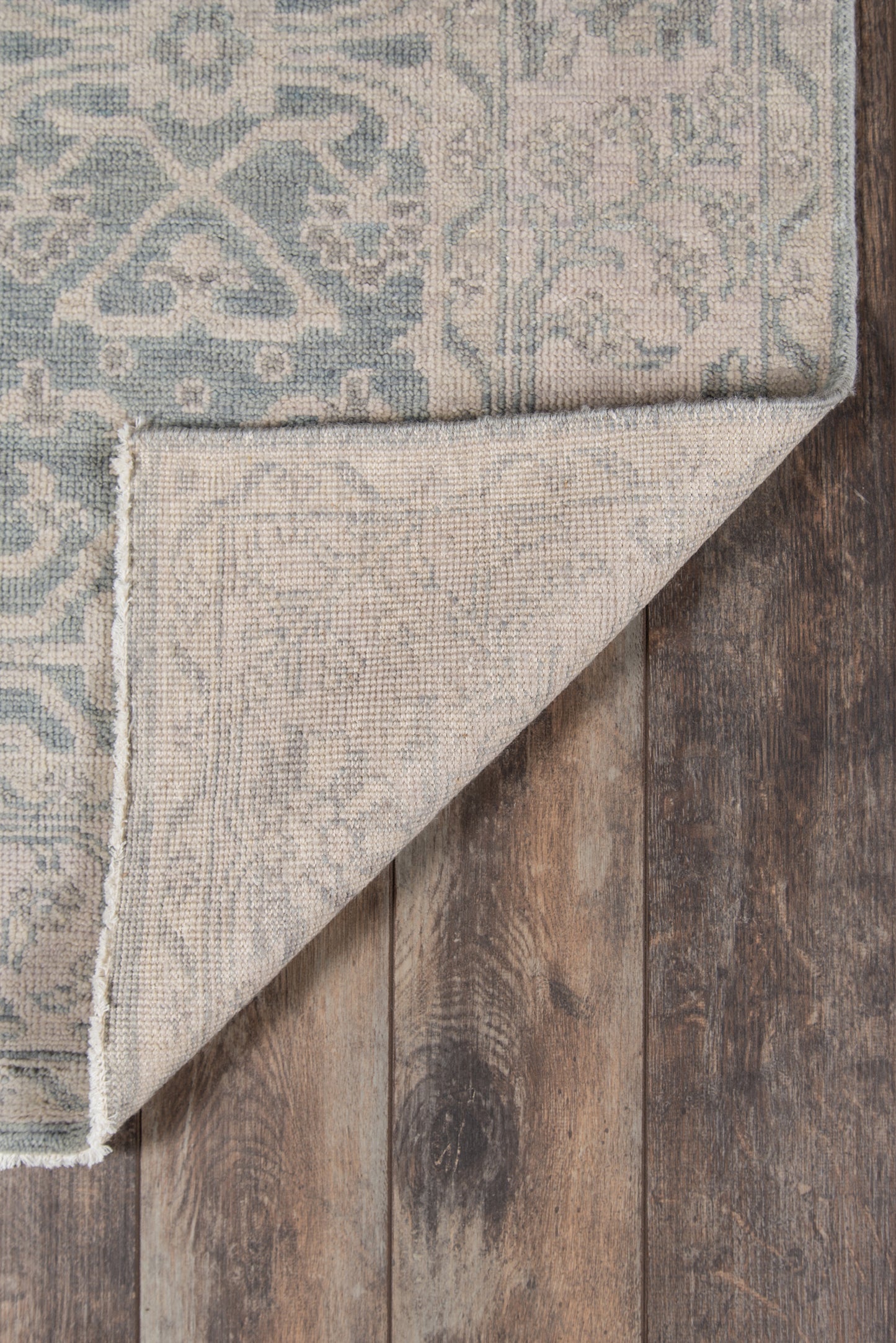 Blue and beige oriental rug with intricate pattern, folded corner reveals lighter back, on dark wood floor.