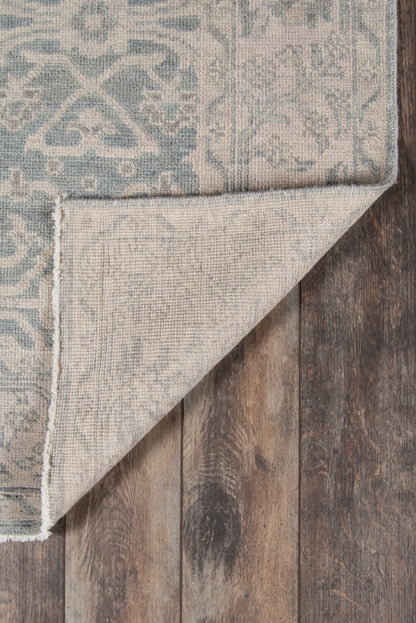 Blue and beige oriental rug with intricate pattern, folded corner reveals lighter back, on dark wood floor.