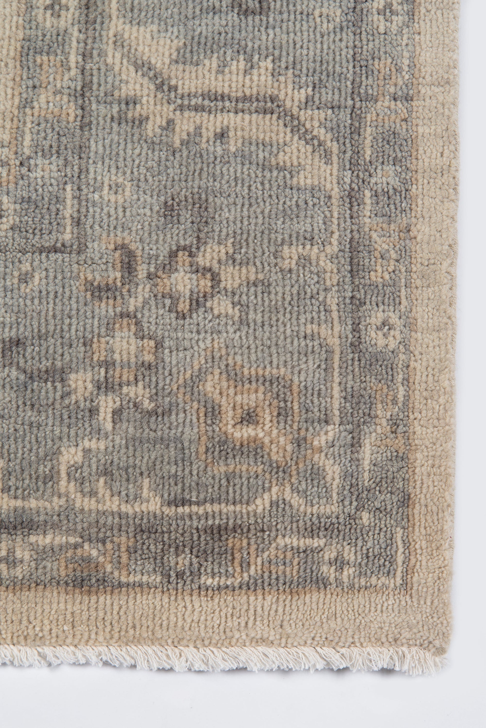 Fringed-edge beige rug with gray-blue arabesque border and cream highlights; soft tufted pile.