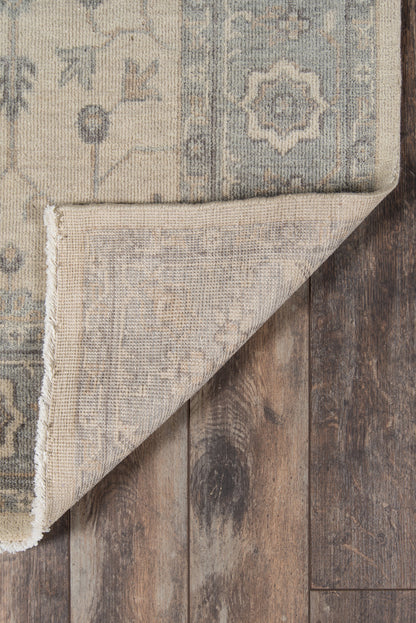 Beige and blue oriental rug with faded medallion pattern; folded corner shows underside on rustic wooden floor.