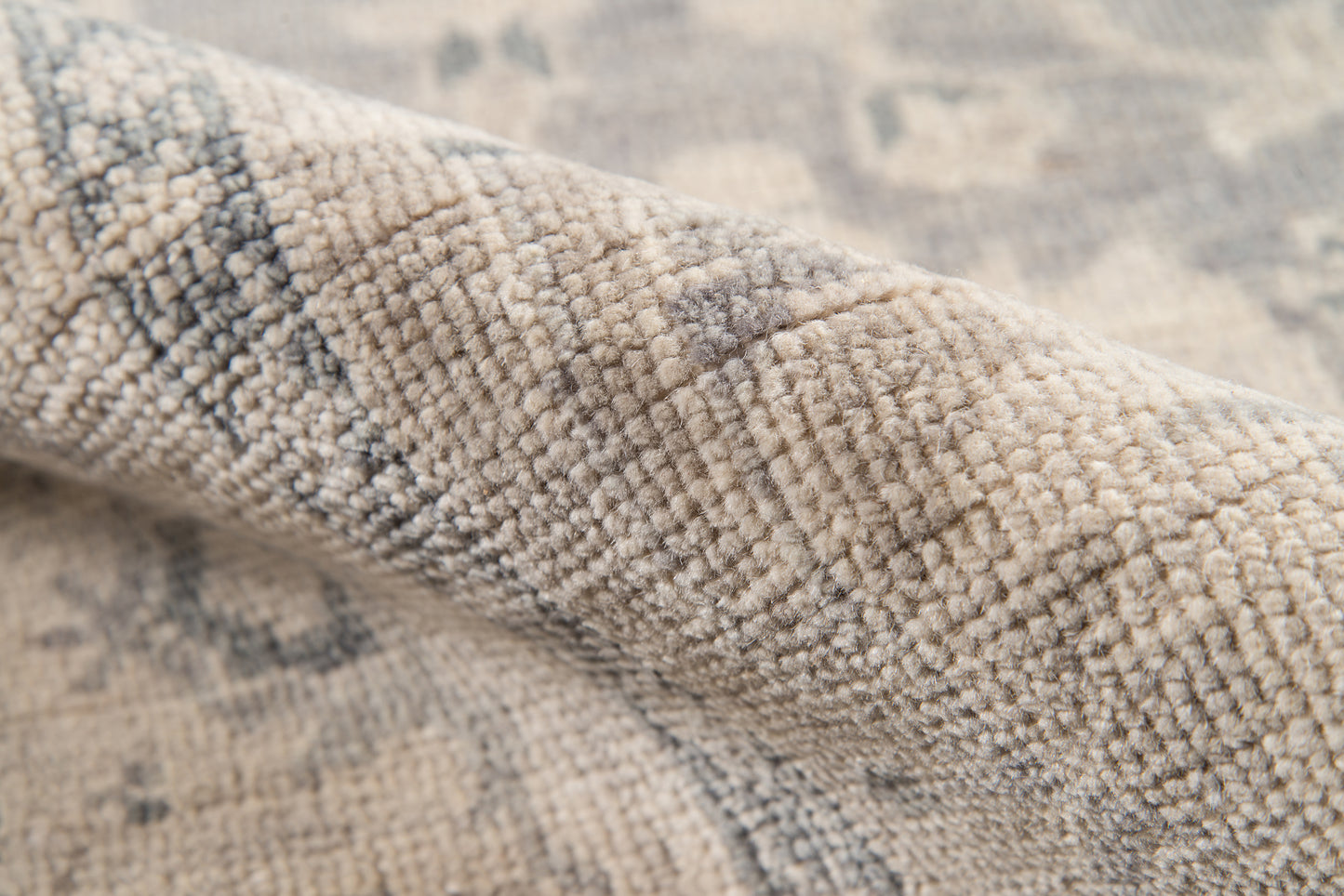 Close-up of beige-gray wool-blend rug with textured loop pile & subtle geometric pattern.
