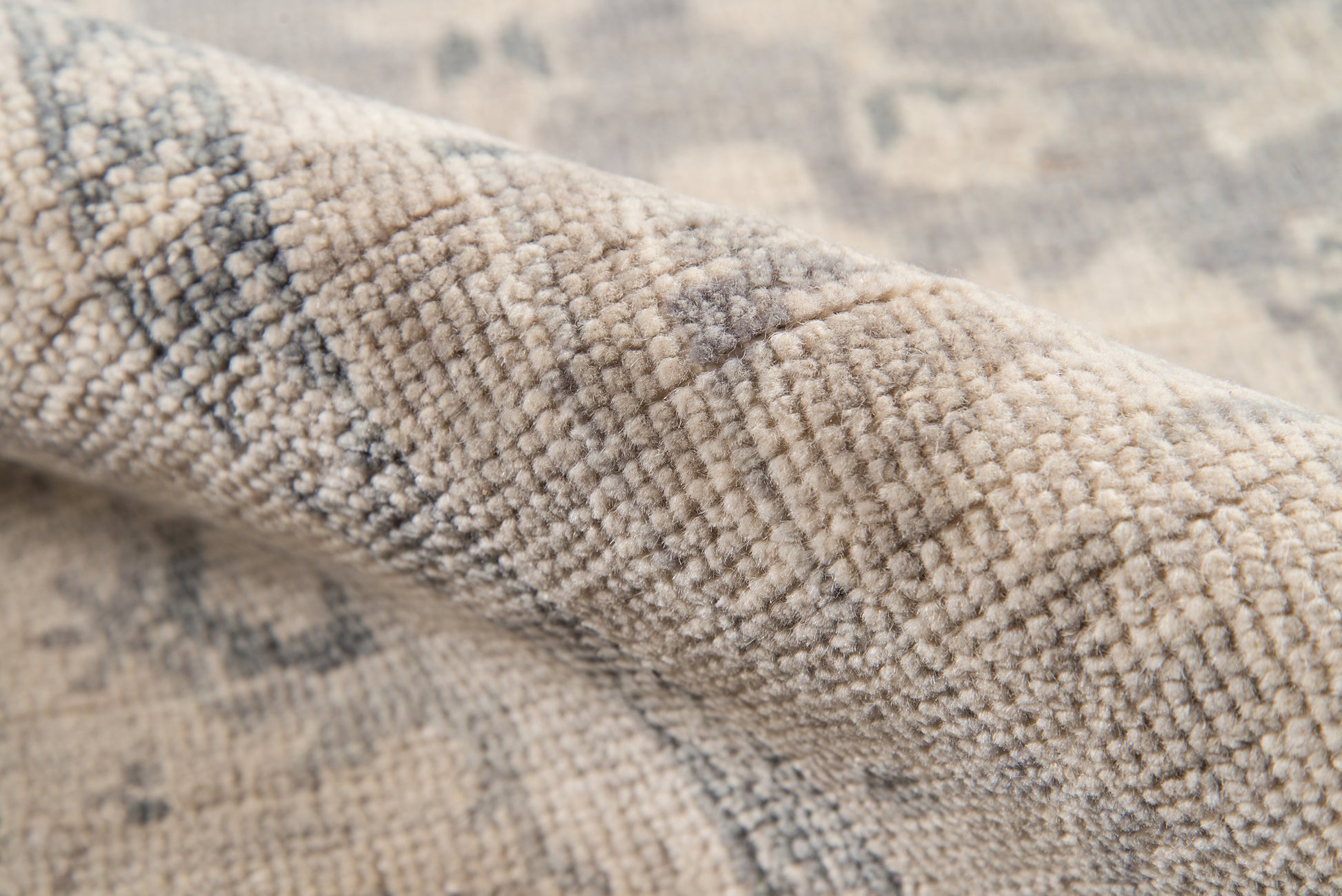 Close-up of beige-gray wool-blend rug with textured loop pile & subtle geometric pattern.