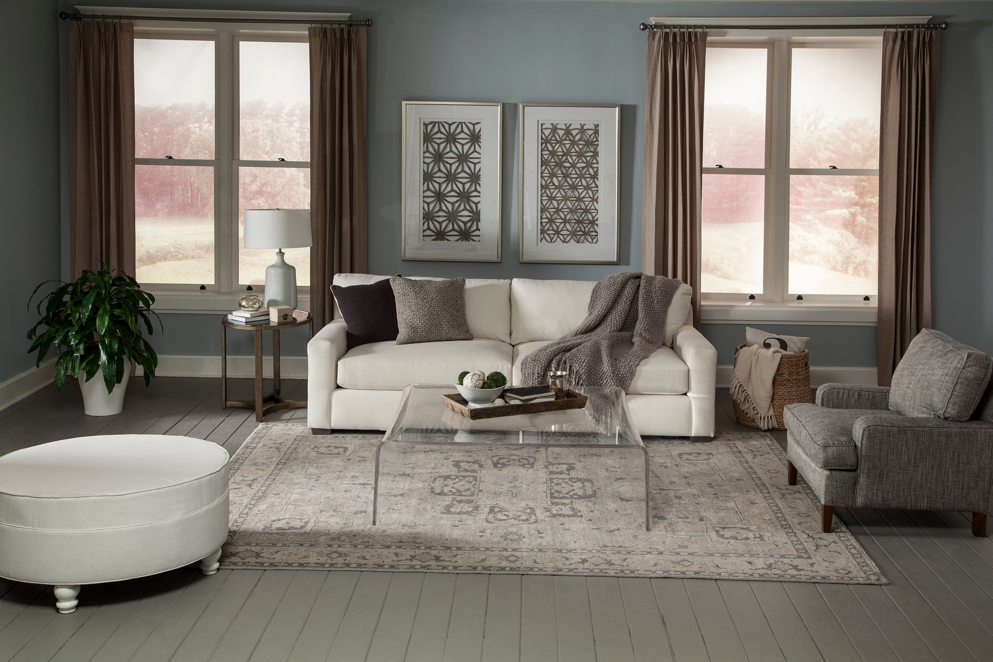 Neutral gray living room with white sofa, gray armchair, transparent acrylic coffee table, soft rug, and framed abstract art.