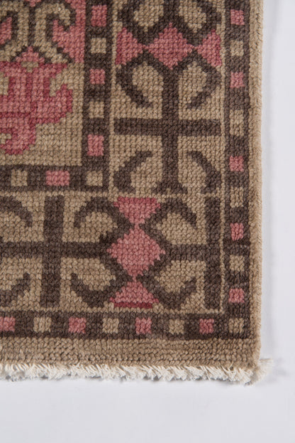 Close-up of a beige-brown geometric tribal rug with pink diamond motifs and fringe along the edge.