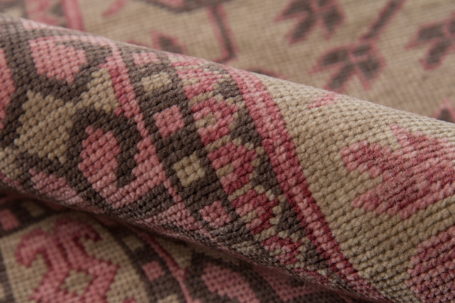 Close-up of a beige woven rug with pink and brown geometric motifs, textured pile, rustic kilim-style decor.