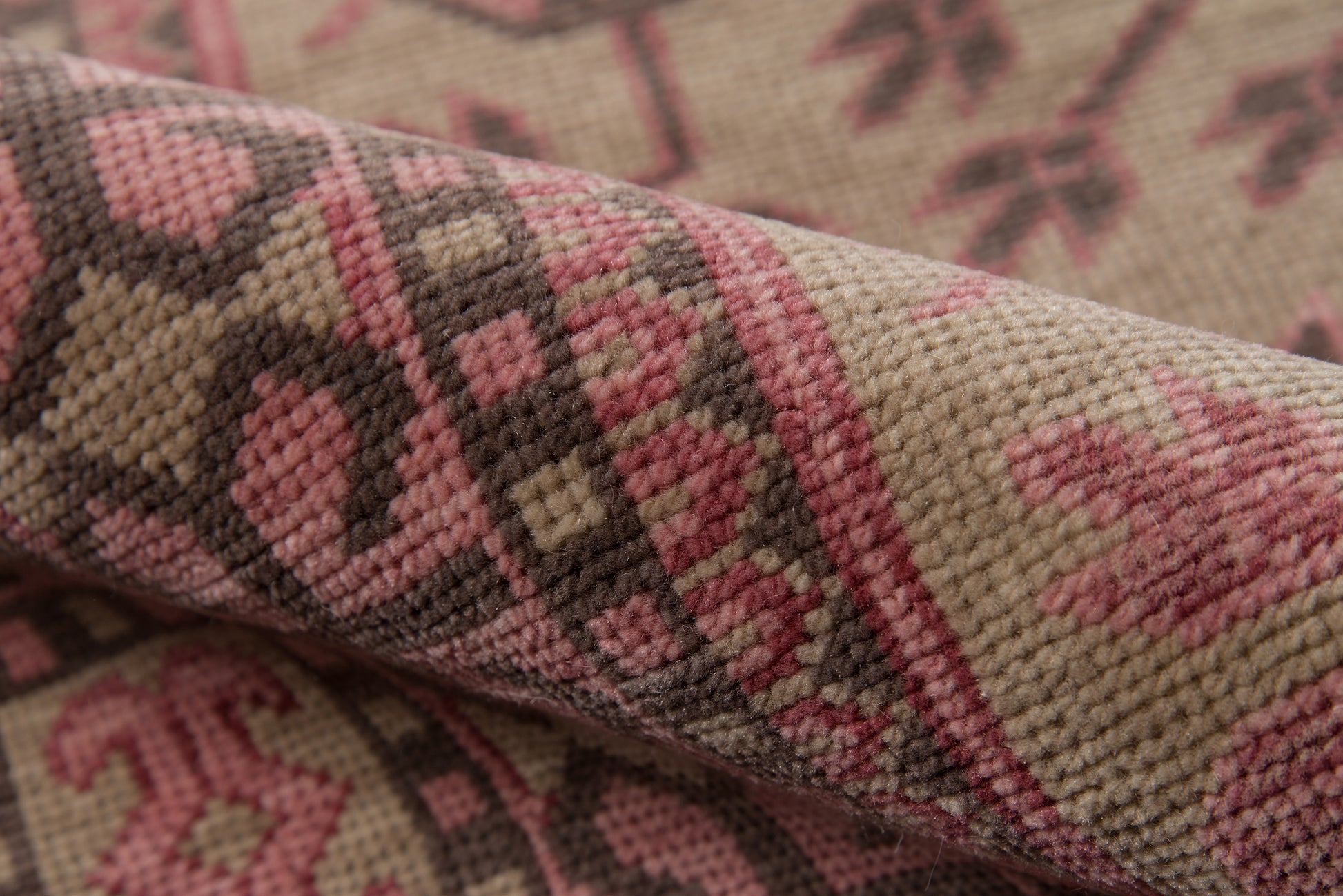 Close-up of a beige woven rug with pink and brown geometric motifs, textured pile, rustic kilim-style decor.