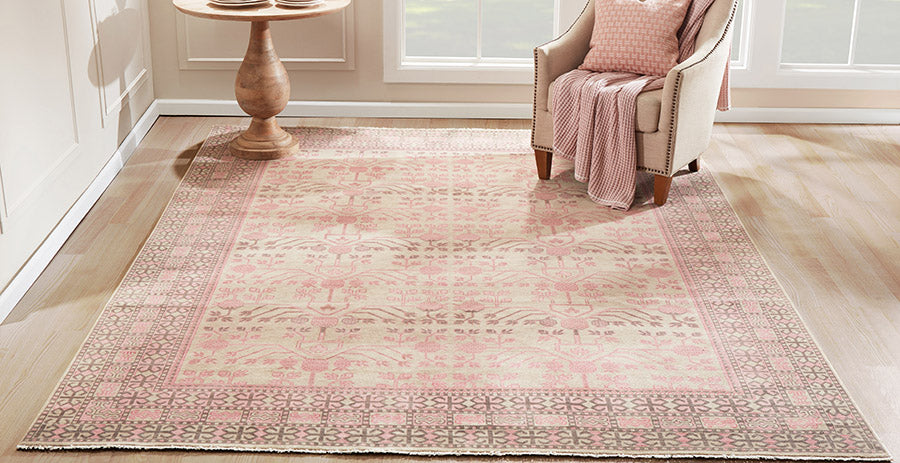Pink and ivory oriental rug on a light wood floor, paired with a beige armchair and pink throw in a sunlit living room.