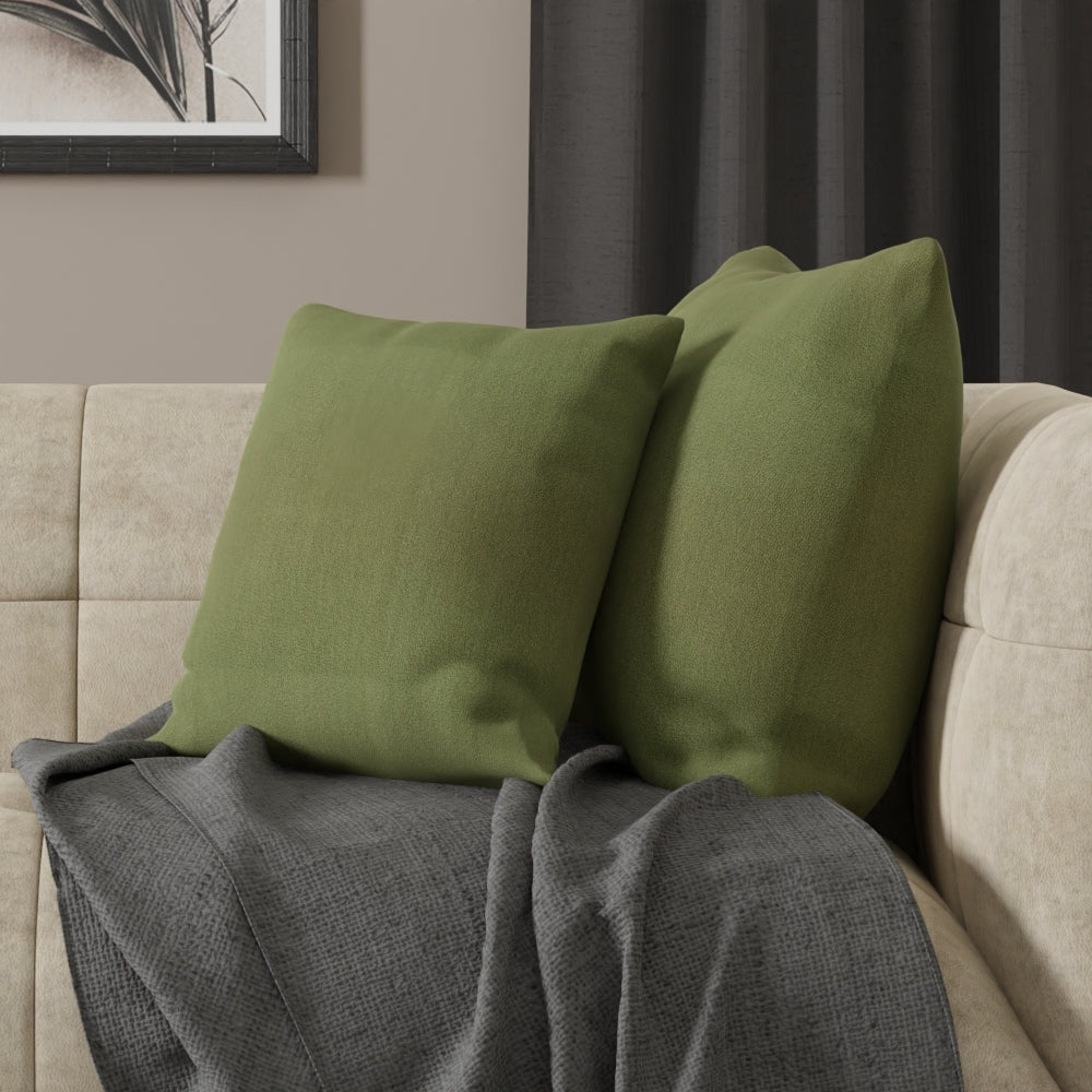 Two olive-green square cushions on a beige sofa with a gray textured throw blanket, modern cozy living room setup.