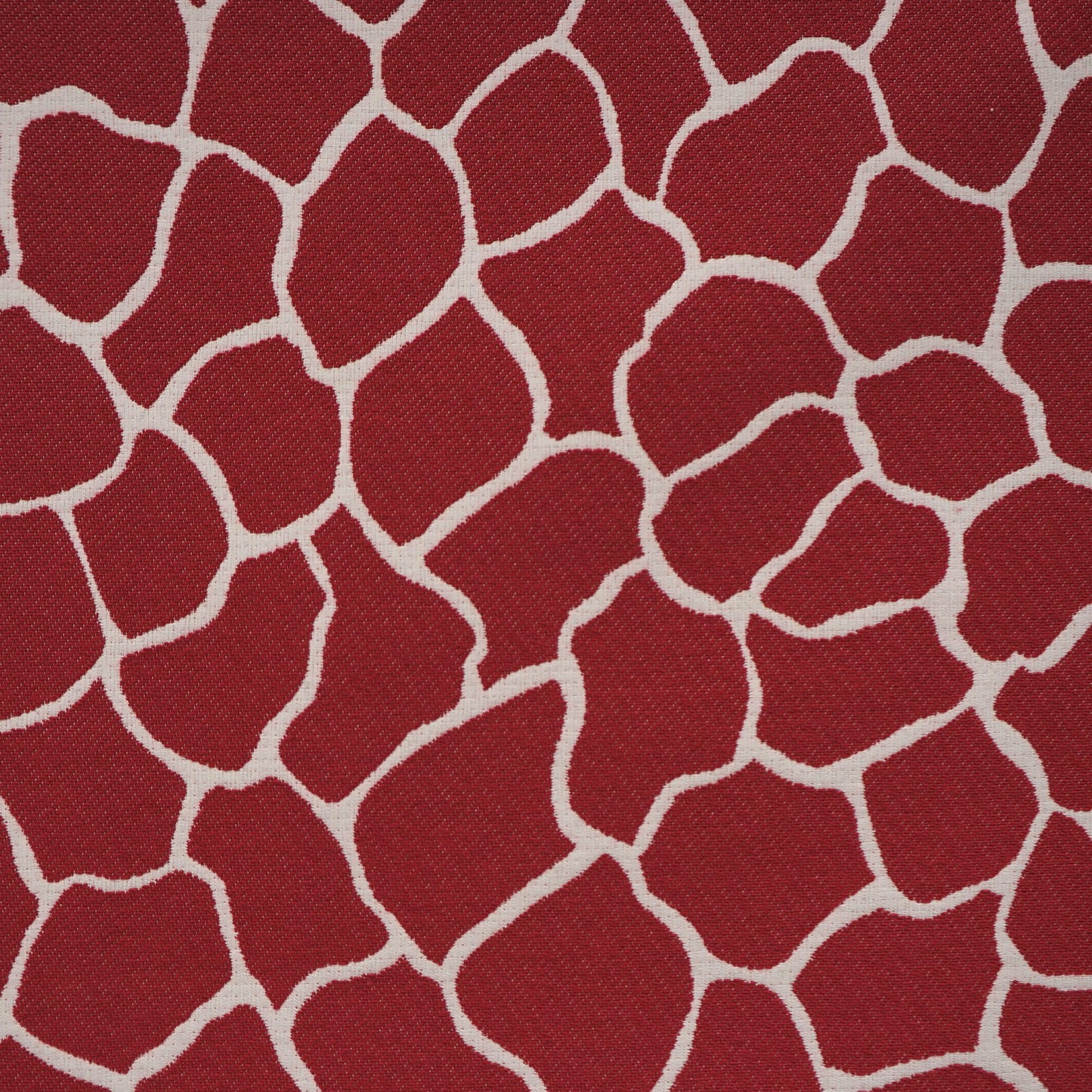 Red woven fabric with irregular white outlines forming a giraffe-like mosaic pattern.