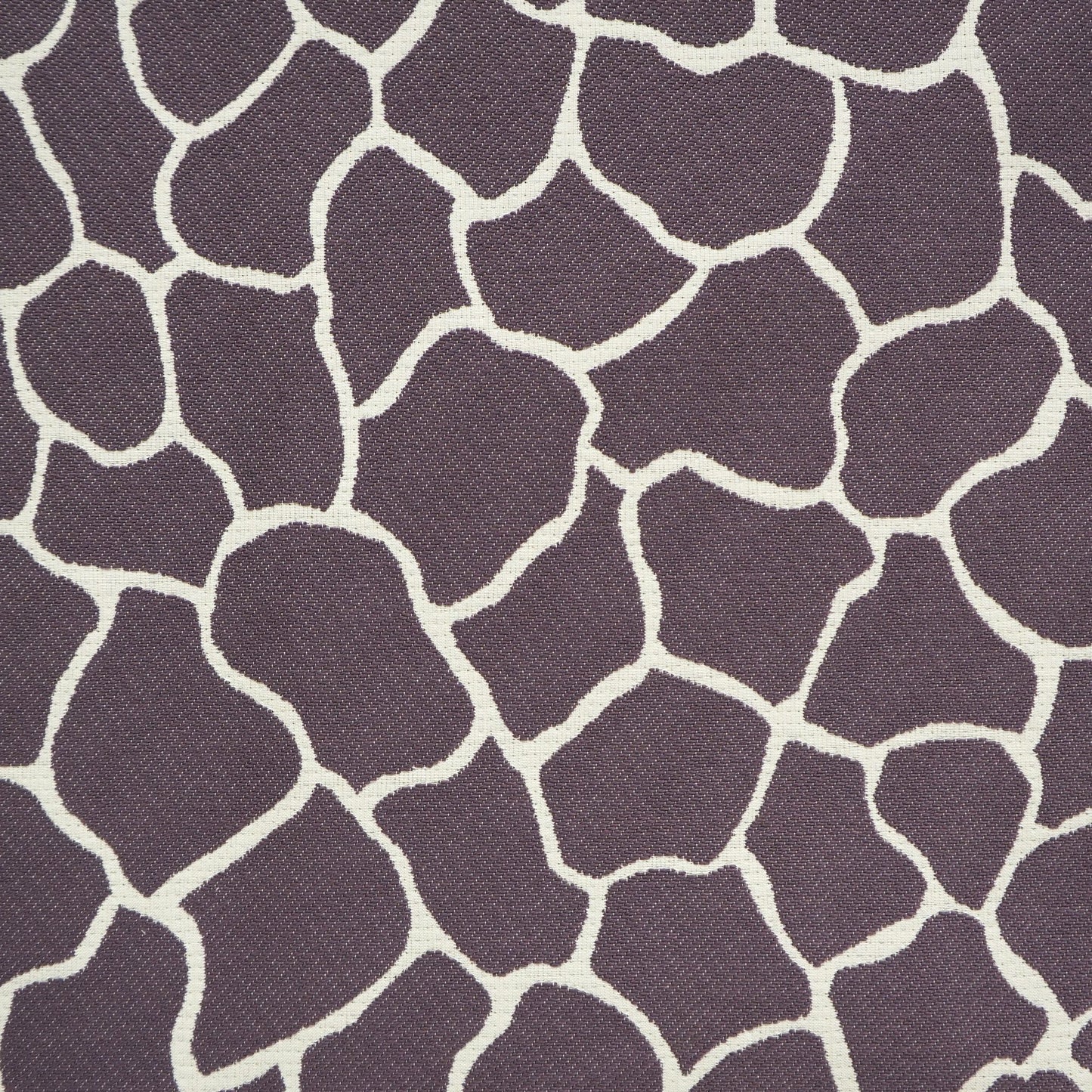 Purple upholstery fabric with cream irregular spots forming a giraffe-like mosaic pattern, textured weave.